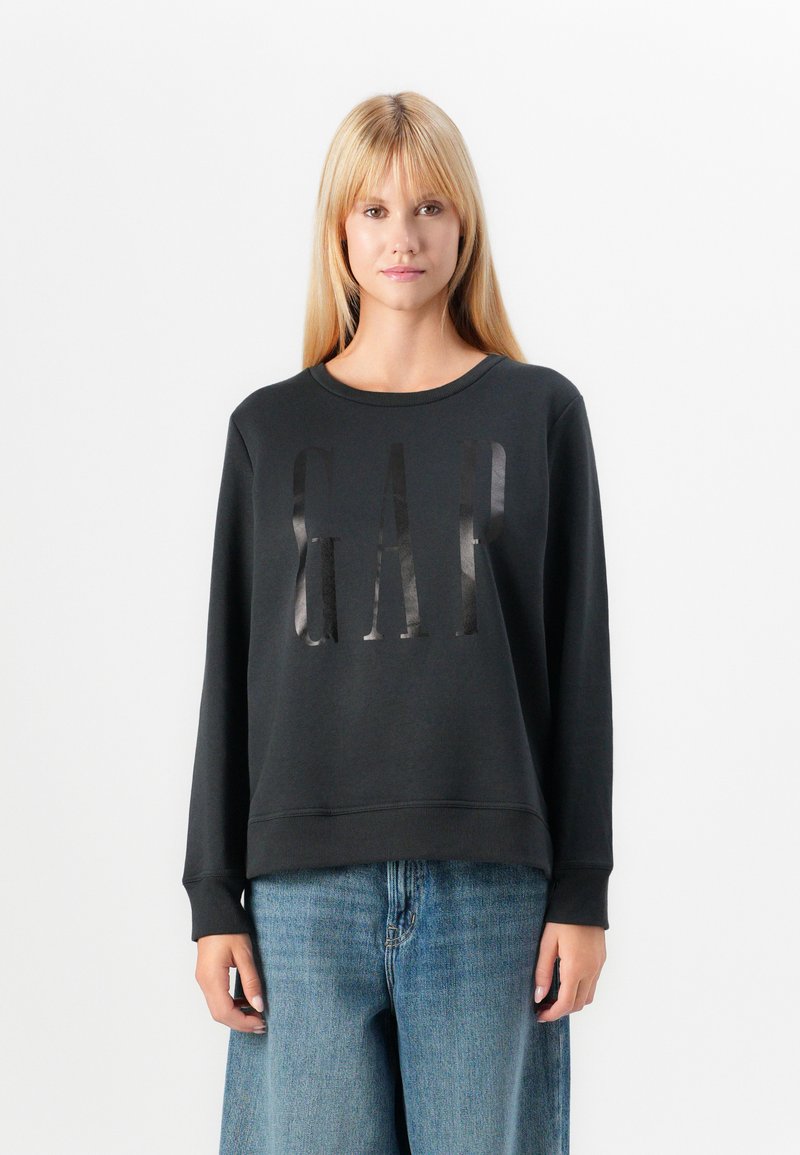 Black sweatshirt with a round neckline and long sleeves, featuring a glossy "GAP" logo on the front. Paired with light blue wide-leg jeans.