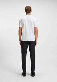 Vit kortärmad polo skjorta med en subtil textur, i kombination med svarta byxor och svarta sneakers, sedd bakifrån.