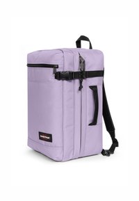 Mochila de tela morada con forma rectangular. Cuenta con un bolsillo frontal con cremallera, correas ajustables y un asa superior. Acabados en negro.