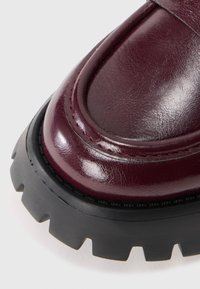 Scarpa in pelle bordeaux con finitura lucida, punta rotonda e suola in gomma nera spessa caratterizzata da battistrada pronunciato e dettagli di cucitura.