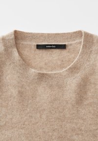 Maglione in lana beige a girocollo con colletto a coste e etichetta nera con la scritta "un giorno" cucita all'interno del collo.