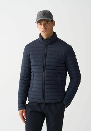 Marine puffer jack met een hoge kraag, horizontaal gestikt oppervlak, ritssluiting aan de voorkant en zijzakken. Gecombineerd met een grijze pet met een logo.