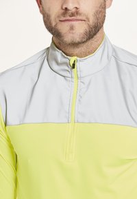 Halv-zip pullover i grå og neon gul, med en glat overflade, en stående krave og en farveblokdesign i kontrast.