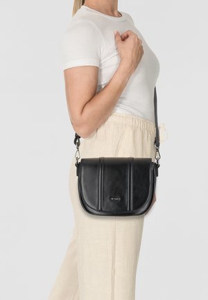 Schwarze Leder-Umhängetasche mit kurvenförmigem Design, ausgestattet mit zwei vertikalen Rillen, verstellbarem Schultergurt und silbernen Hardware-Details.