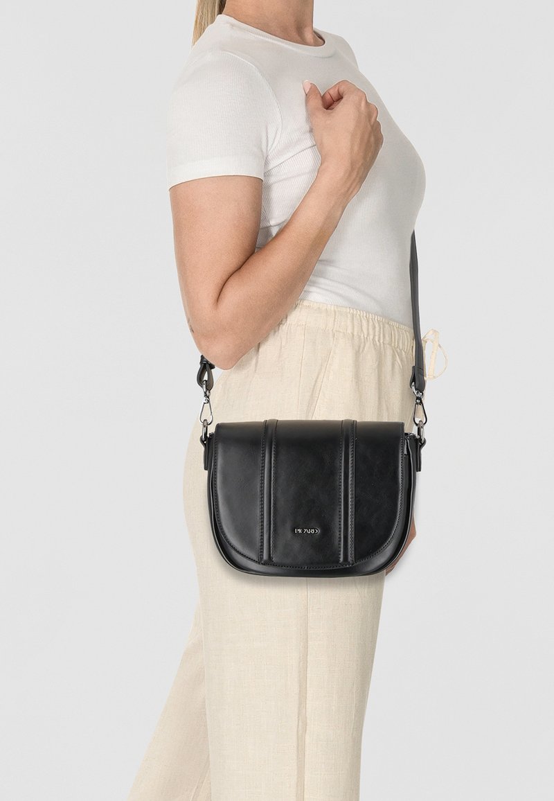 Schwarze Leder-Umhängetasche mit kurvenförmigem Design, ausgestattet mit zwei vertikalen Rillen, verstellbarem Schultergurt und silbernen Hardware-Details.
