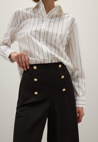 Witte gestreepte overhemd met knopen en een kraag, gecombineerd met hoge zwarte broeken met gouden knopen en een getailleerd ontwerp.