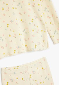 Sæt af lysegult tøj med ribbet tekstur, der har et blomsterdesign i pink, blå og gul. Inkluderer en langærmet top og matchende bukser.