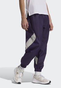 Námornícke teplákové nohavice so sivým bočným panelom, elastickými manžetami a ľahkým materiálom. Nosené s bielymi teniskami s grey akcentmi.