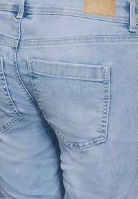 Vaqueros de mezclilla azul claro con dos bolsillos traseros con costuras visibles y una pequeña etiqueta de cuero marrón cerca de la cinturilla.