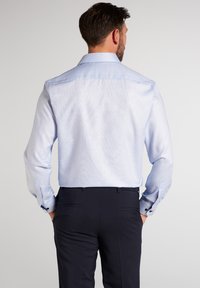 Helles blaues Langarmhemd aus weichem Material, mit einem klassischen Kragen und kontrastierenden Knöpfen an den Manschetten, kombiniert mit dunklen Hosen.