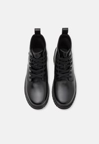 Botas de cuero negro hasta el tobillo con una textura suave, puntera redonda, cordones en la parte frontal y tiradores en el talón para facilitar su colocación.