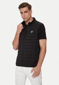 Gilet imbottito nero con colletto alto, zip frontale e tasche laterali con zip, realizzato in materiale leggero e con un design elegante e rettangolare.