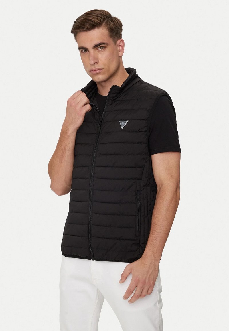 Gilet imbottito nero con colletto alto, zip frontale e tasche laterali con zip, realizzato in materiale leggero e con un design elegante e rettangolare.