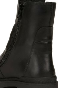 Botín negro de cuero con cremallera lateral, textura suave, puntera redonda y suela de goma resistente. Detalles con un diseño de costura sutil.