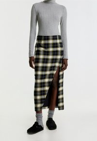 Grauer gerippter Langarmshirt kombiniert mit einem schwarzi-gelben Karo-Maxirock mit einem vorderen Schlitz. Schwarze Slipper und graue Socken sichtbar.