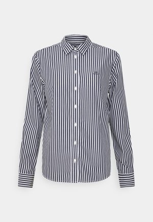 Chemise à manches longues boutonnée avec des rayures verticales noires et blanches et un petit logo brodé sur la poitrine gauche.