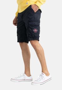 Shorts cargo marine avec plusieurs poches, une poche à rabat sur le côté et un patch circulaire rouge avec le numéro "73" sur la cuisse.