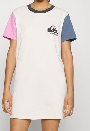 Person trägt ein weißes Kleid mit pinkem linken Ärmel, blauem rechten Ärmel, schwarzem Kragen und Quiksilver-Logo auf der linken Brust.