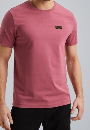 T-shirt à manches courtes et col rond en coton rose poussière avec un petit label noir sur la poitrine gauche. Texture lisse.