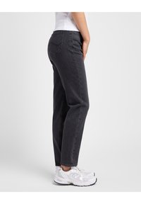 Jeans de mezclilla negra con un corte ajustado, que cuentan con un diseño clásico, bolsillos delanteros y bolsillos traseros tipo parche. Combinados con zapatillas deportivas blancas.