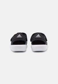 Black fabric sandals with white rubber soles and three horizontal stripes. Features adjustable straps and visible Adidas logo.