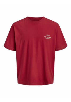 Dreng iført en rød T-shirt, løse blå jeans og brune sko, står og kigger til venstre med et let smil.