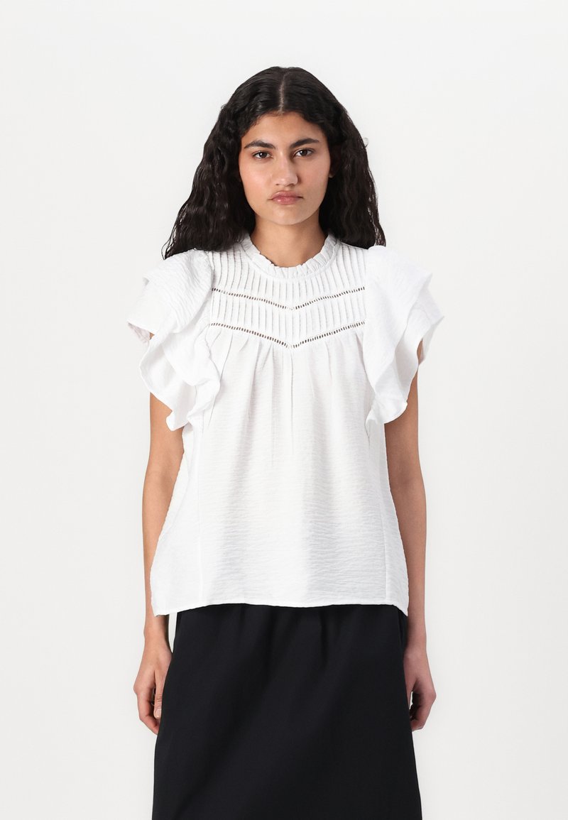 Blouse blanche à manches courtes avec des manches volantées, tissu texturé et plis horizontaux le long de l'encolure. Associe à une jupe noire.