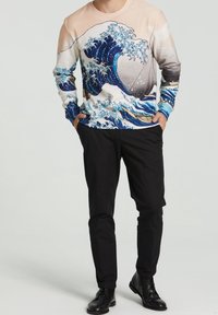 Felpa a maniche lunghe con un design a onde blu e bianche, con una parte superiore di colore rosa chiaro. Indossata con pantaloni e scarpe nere.