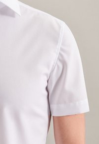 Camicia bianca a maniche corte con colletto classico, realizzata in morbido tessuto di cotone, caratterizzata da un aspetto pulito e sartoriale e dettagli di cucitura discreti.
