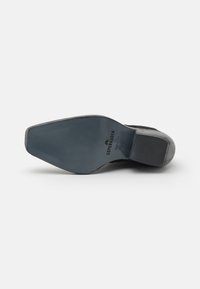Suela de zapato de ante negro con una textura suave. Tacón ligeramente texturizado y logo grabado "Copenhagen" en la plantilla. Forma plana y acanalada.