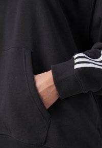 Sudadera negra con bolsillo tipo canguro, con acentos de rayas blancas en las mangas. Fabricada con un tejido suave y texturizado, con un corte relajado.