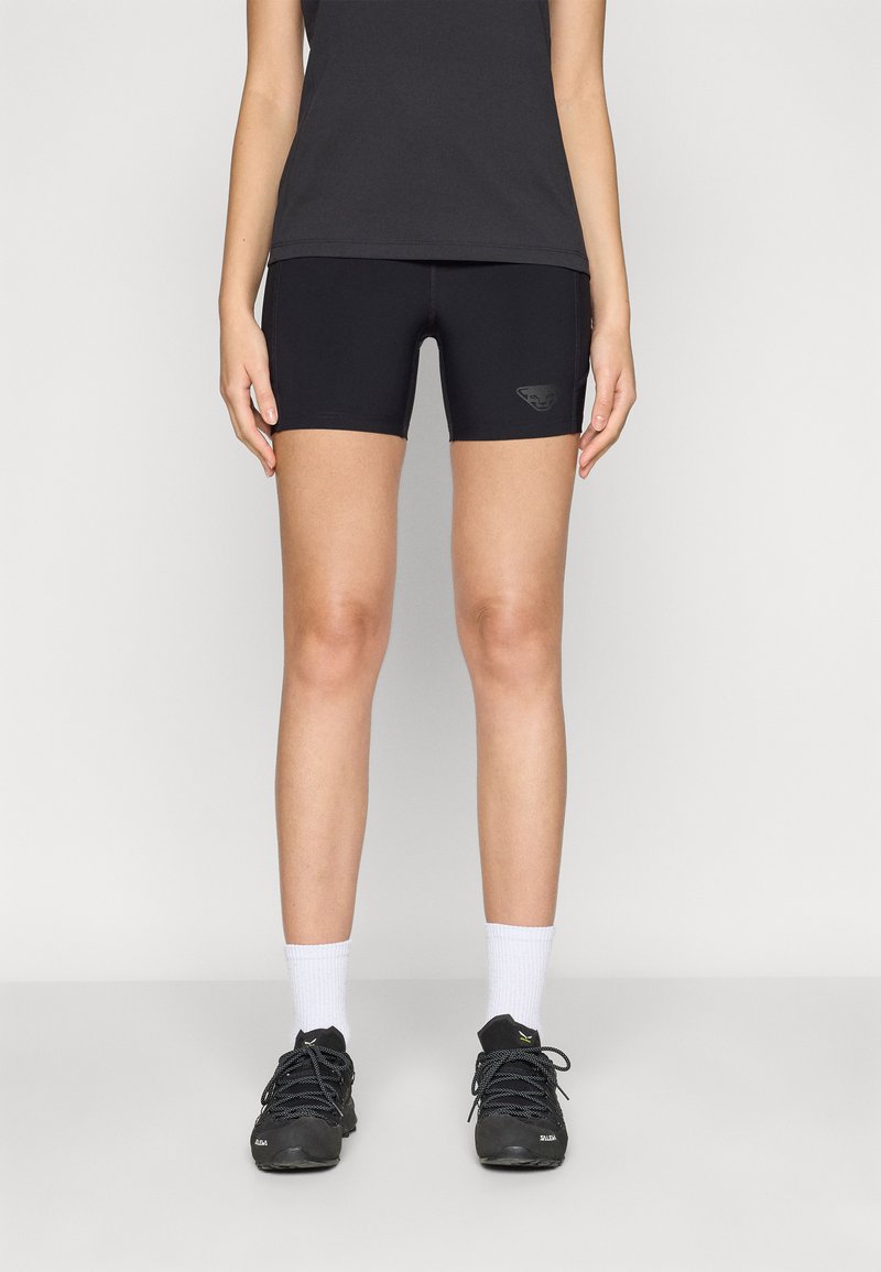 Pantaloni sportivi neri con un design aderente, dotati di un logo discreto sul davanti. Indossati con scarpe nere e calzini bianchi alla caviglia.