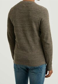 Brauner Strickpullover mit langen Ärmeln, rundem Ausschnitt und strukturiertem Finish. Getragen mit blauen Jeans, die einen lässigen Schnitt und Stil zeigen.