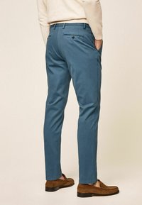 Light blue cotton trousers with a tailored fit, featuring back pockets and subtle seams. Worn with brown suede loafers.