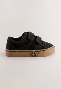 Melns auduma sporta apavu pāris ar divām Velcro aizdarēm, gumijas zoli un smaidīgo sejiņas uzliku uz sāna. Virspuse ar teksturētu materiālu un sānu šuvju detaļām.