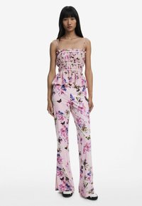 Salopette floreale in tessuto rosa con corpetto aderente, dettaglio peplum e pantaloni a campana. Presenta colorati motivi di farfalle e fiori.