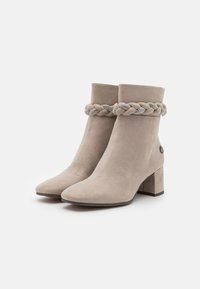 Bottines en suède beige clair avec un accent tressé au niveau du col, ornées d'embellissements métalliques et d'un large talon bloc.