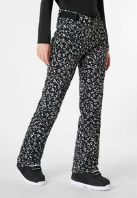 Zwarte sneeuwbroek met een wit bloemenpatroon, voorzien van een hoge tailleband en zakken, gecombineerd met zwarte laarzen. Gelaagd en gewatteerd materiaal.