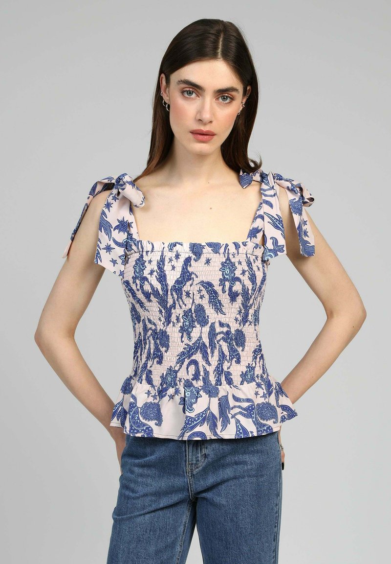 Haut peplum rose clair avec un motif floral bleu, décolleté carré et bretelles à nouer. Dispose d'un panneau smocké et d'un ourlet froncé. Porté avec un jean.