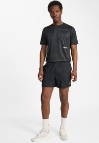 Svart atletisk outfit bestående av en texturerad kortärmad tröja och shorts. Båda har ett subtilt mönster och har resår i midjan.