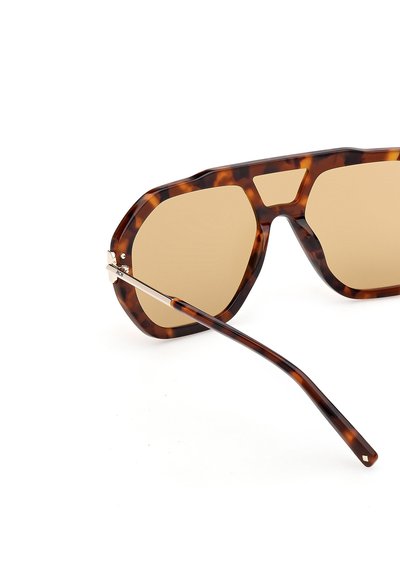 Lunettes de soleil oversize en écaille de tortue avec des verres teintés marron et un détail de charnière en métal sur la branche, sur fond blanc.