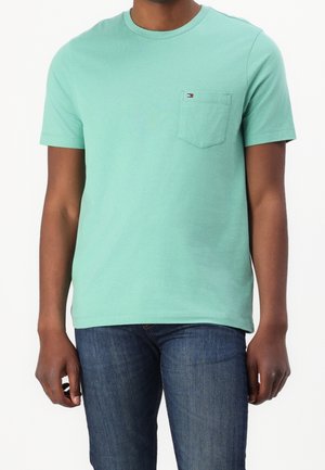 Minttu vihreä lyhythihainen t-paita, jossa on pyöreä kaula-aukko ja vasemmalla rintatasku, jossa on pieni logotagi. Yhdistetty tummansinisiin farkkuihin.