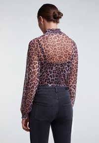 Transparent, støvet lyserød bluse med leopardprint, høj halsudskæring, elastiske manchetter; kombineret med mørke bukser i høj talje med baglommer.