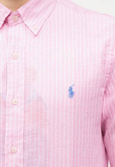 Ροζ και λευκό κάθετα ριγέ πουκάμισο με κουμπιά και μπλε κεντημένο λογότυπο παίκτη πόλο στο αριστερό στήθος.
