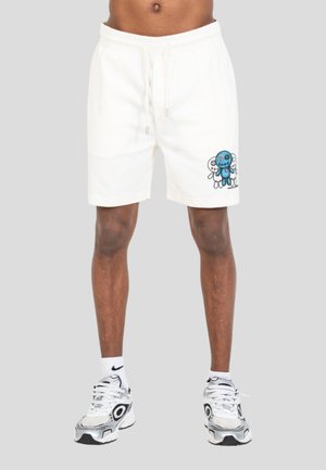 Pantaloncini bianchi con una grafica di un personaggio dei cartoni animati blu e bianco sulla gamba destra, indossati con calzini Nike bianchi e scarpe da ginnastica bianche.