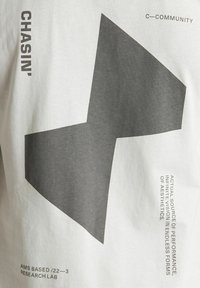 Grijze en witte katoenen t-shirt met een grote asymmetrische grijze grafiek. De tekst bevat "CHASIN'" en "C-COMMUNITY" in zwarte druk.