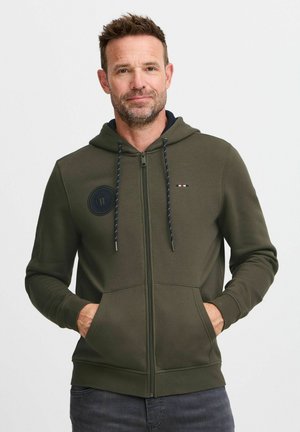 Sudadera con cremallera en verde oliva, fabricada en una mezcla de algodón, que presenta un diseño de parche redondo, capucha con cordones en azul marino y bolsillos frontales.