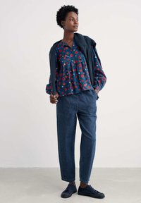 Bluzka w kwiaty w kolorze granatowym z czerwonymi kwiatami, lekko falbaniasta; w zestawieniu z luźnymi niebieskimi dżinsami i ciemnymi trampkami.
