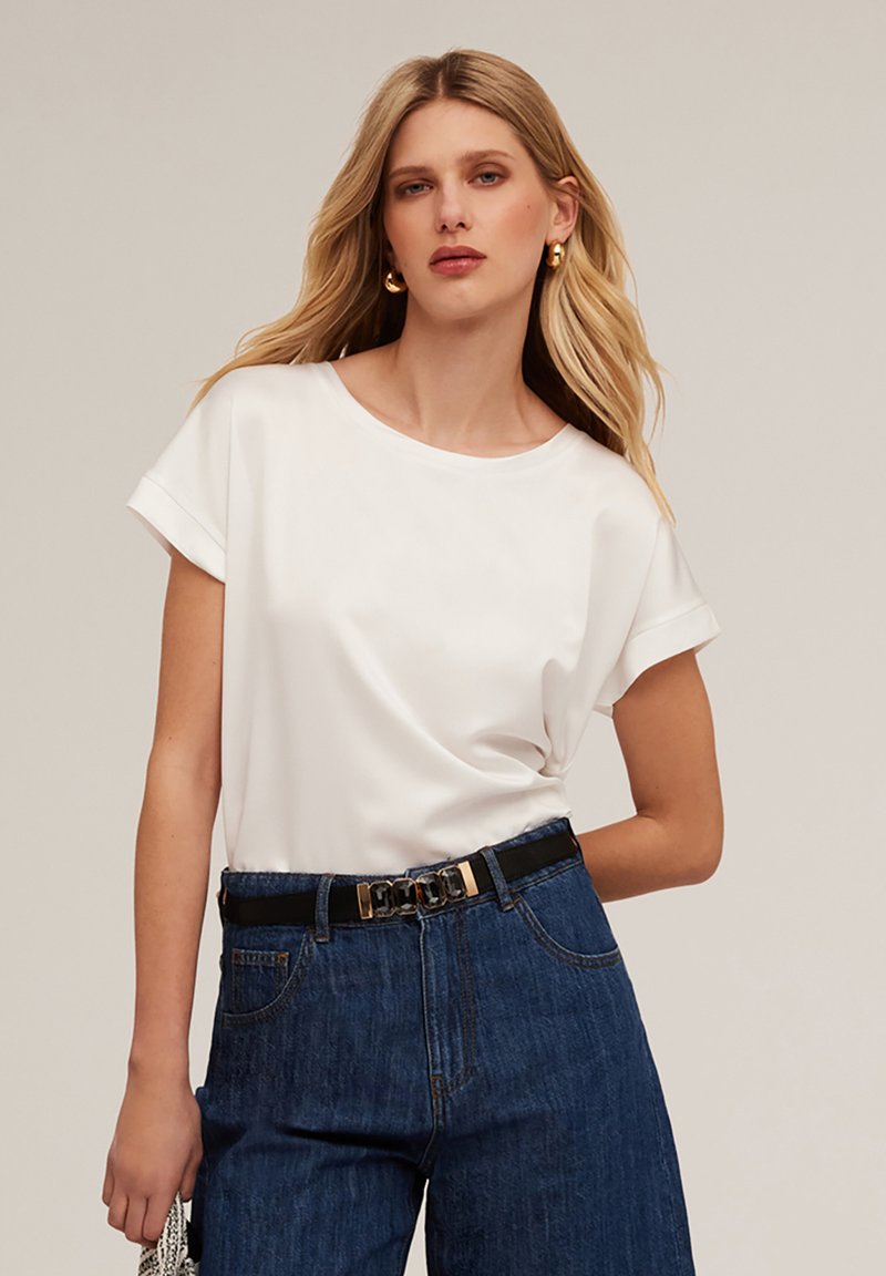 Top alb cu mânecă scurtă și decolteu rotund, purtat cu pantaloni din denim cu talie înaltă, care au o curea neagră cu accente metalice.