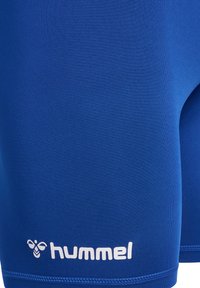 Blå sportshorts i elastisk tyg, med en mjuk textur och en vit logotyp längst ner. Närbild av material och sömmar.